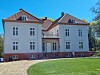 Stor hvit bygning med rød tegltak og mange vinduer ved en grønn plen.