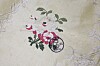 Lite, brodert blomstermotiv i rosa og grønt på lys tekstil.