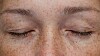 Nærbilde av lukkede kvinneøyne i et ansikt med fregner.