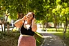 Ung kvinne med hodetelefoner står i en grønn park og lytter til musikk.