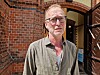 Portrett av Arne Jor foran kirke med buet inngang og åpne dører.