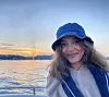 Portrettbilde av en smilende Hijab Fatima Ali. Hun er på en båt og har på seg en flytevest, og en båthatt i olastoff på hodet. I bakgrunnen ser vi havet og en solnedgang.