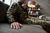 Nærbilde av en soldat i kamuflasjeuniform som sitter i en sofa i en stue.
