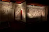 Et opplyst etruskisk gravkammer med veggmalerier og åpne dører i et mørkt museumsrom.