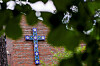 Rødtvet kirke med murfasade og blå korsmotiv, delvis skjult av grønne blader.