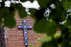 Rødtvet kirke med murfasade og blå korsmotiv, delvis skjult av grønne blader.