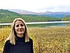 Kvinne står foran en innsjø med skogkledde fjell i bakgrunnen