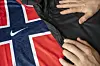 Nærbilde av Norges røde, hvite og blå fotballdrakt med Nike-logo, og med motiv fra Urnes stavkirke To hender holder over stoffet.