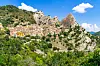 Castelmezzano ligger tett mellom grønne åser og spisse, dramatiske fjell under en blå himmel.