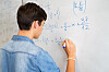 Elev i dongeriskjorte skriver algebraiske uttrykk på en whiteboardtavle.