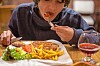 Gutt spiser kotelett med pommes frites og ketchup ved et restaurantbord.