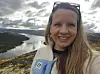 Erin Lindsay smiler foran en innsjø med skogkledde fjell og skyer.