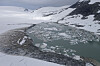 Snødekt brelandskap med et grønnlig smeltevannsbasseng og flytende isflak.