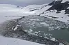 Snødekt brelandskap med et grønnlig smeltevannsbasseng og flytende isflak.