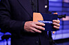 Programleder i NRK ikledd mørk dress holder et oransje kort med teksten «Debatten» i et studio-lignende miljø.